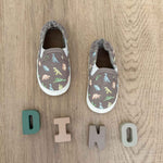 Pair of children's dinosaur shoes on a wooden floor with 'DINO' spelled out below.